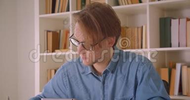 戴眼镜的有魅力的白种人男学生在办公室室内使用平板电脑做笔记的特写照片